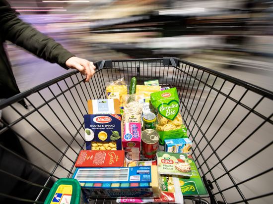 Ein Einkaufswagen wird durch einen Supermarkt geschoben. Die immer billiger werdenden Preise für Lebensmittel stehen in der Kritik.