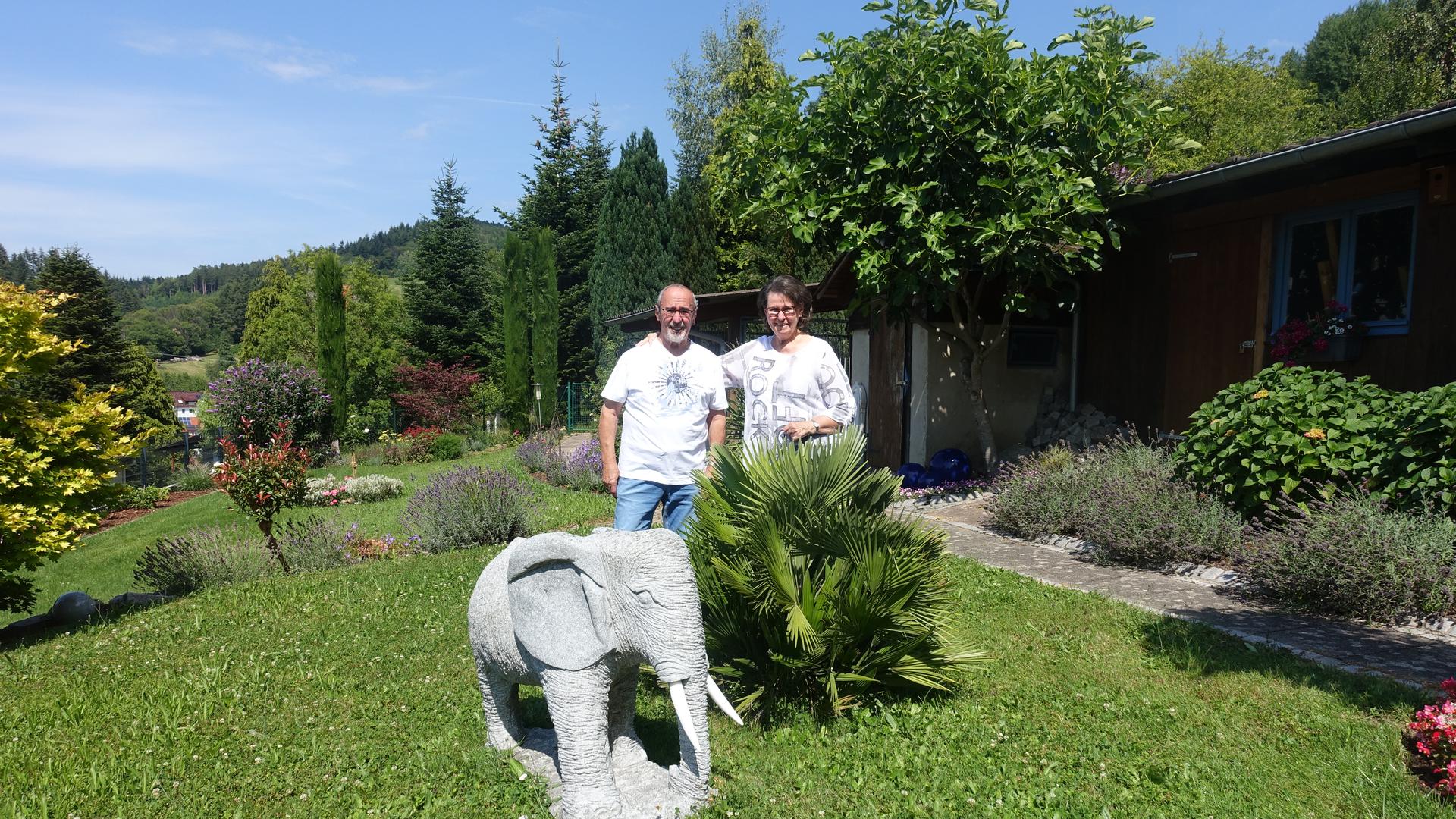 Ein Ehepaar steht nebeneinander in einem Garten an einem Stein-Elefanten.