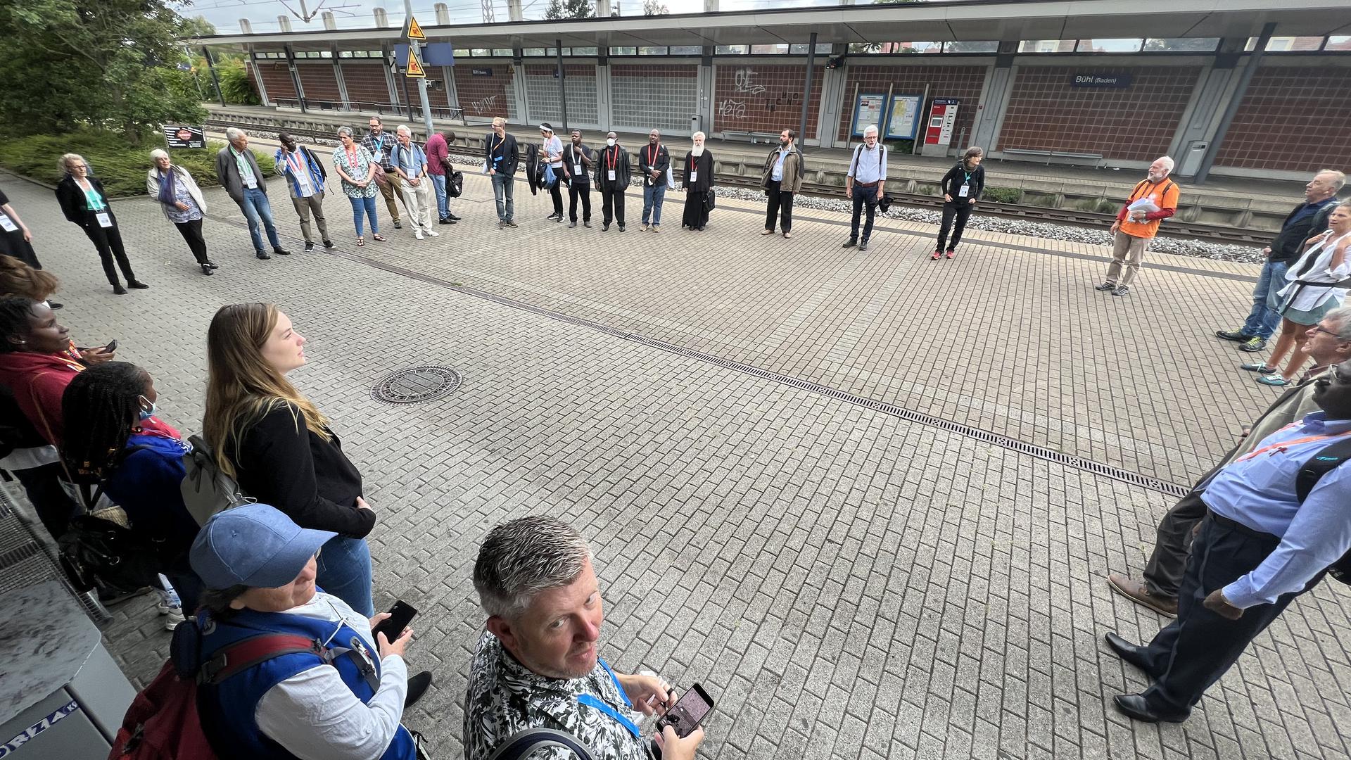 Eine Gruppe Menschen steht an einem Bahnhof.