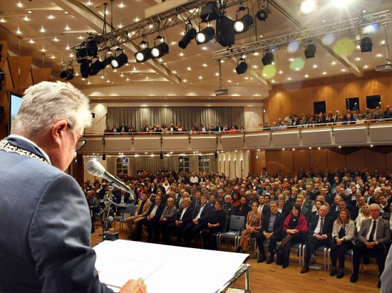 Ein Mann steht am Rednerput vor einem vollen Saal.