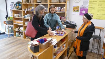 Szene in einem Laden. Eine Frau und ihre Tochter werden von einer Verkäuferin bedient. 