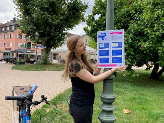 Stadt-Mitarbeiterin Lisa Mulyk bringt ein Plakat für die Excape-Tour beim Stadtgarten an.