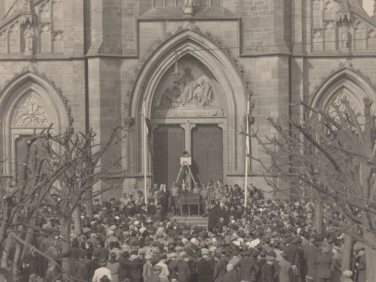 Das Schwarz-weiß-Bild zeigt eine Menschenmenge vor einer Kirche.