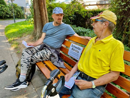 Zwei Männer sitzen auf einer Parkbank. 