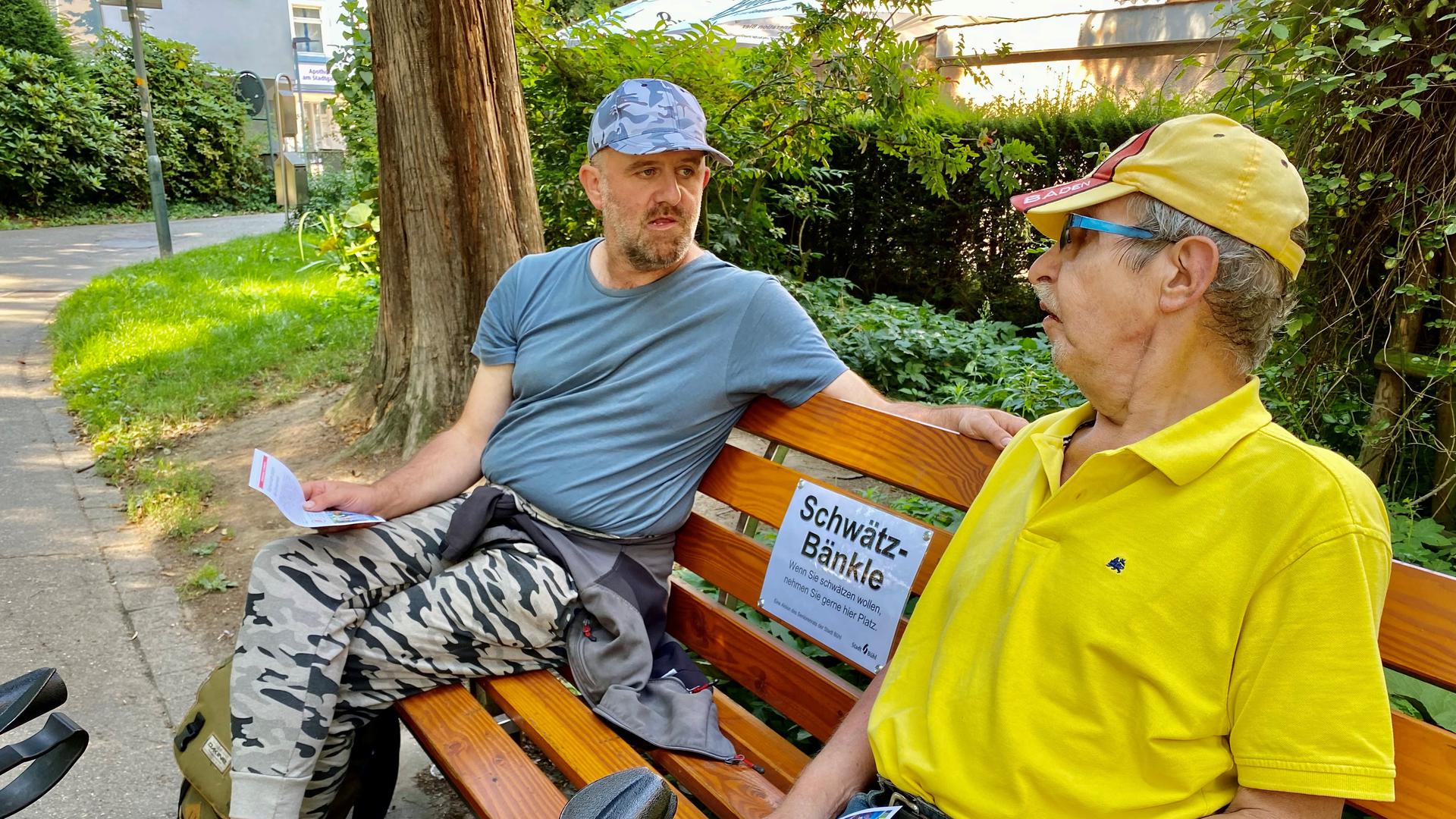 Zwei Männer sitzen auf einer Parkbank. 