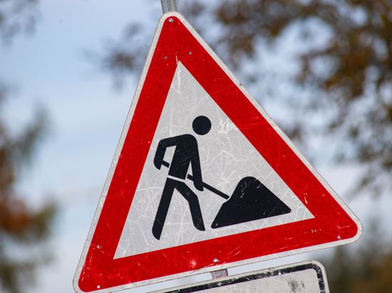 Ein zerkratztes Schild mit dem Gefahrzeichen Arbeitsstelle steht vor einer Baustelle.