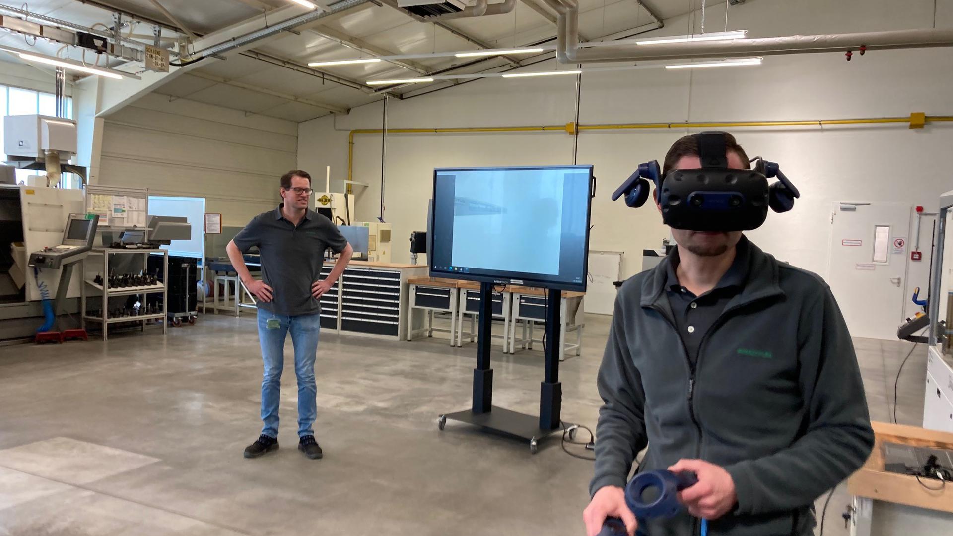Ein Schaeffler-Mitarbeiter bewegt sich mit Virtual Reality durch das geplante neue Ausbildungszentrum. Der Ausbildungsleiter Sascha Kamm erklärt die bewegten Bilder auf dem Bildschirm. 