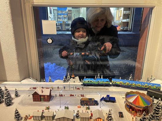 Kind und Oma schauen durch ein Fenster auf eine Modelleisenbahn
