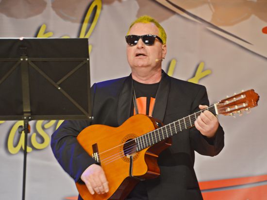 Ein Mann mit Sonnenbrille und Gitarre steht vor einem Pult