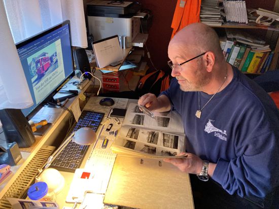 Thomas Kohler am Schreibtisch mit Lupe, alte Fotos von Eisenbahnen betrachtend