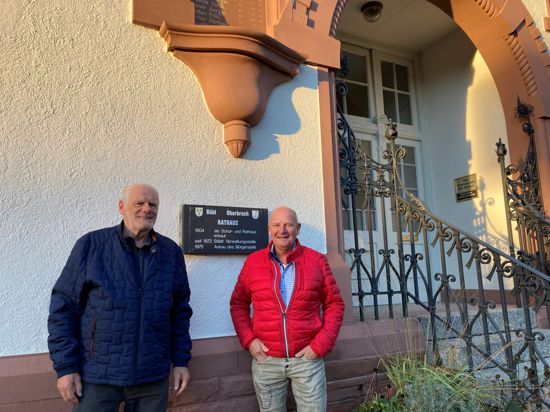 Zwei Männer stehen vor dem Eingang eines historischen Hauses, an dem eine Tafel „Rathaus Oberbruch“ zu sehen ist.