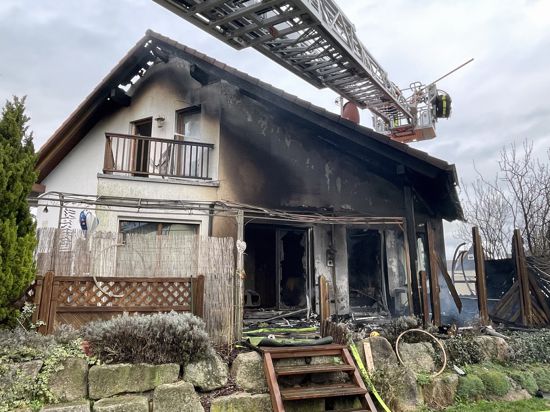Eine Drehleiter schwebt über ein durch Feuer beschädigtes Haus