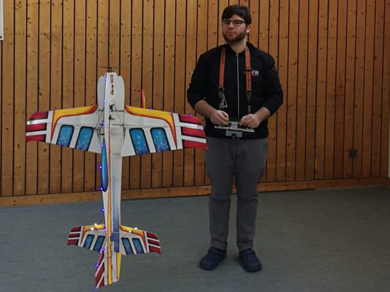 Ein Mann mit Bart, Brille und Fernsteuerung steht neben einem Modellflugzeug