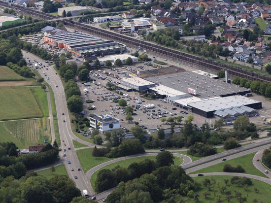 Luftaufnahme des Supermarkt-Gebäudes und umliegender Gebäude mit der Bahnlinie im Hintergrund