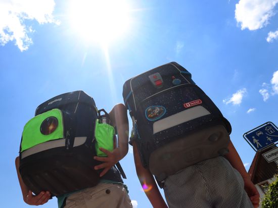 Zwei Kinder laufen mit ihren Büchertaschen im Sonnenschein. Anspruch auf Hitzefrei hat kein Kind. Die heutigen Regelungen dazu sind von Bundesland zu Bundesland unterschiedlich. (zu dpa "Früher gab's Hitzefrei - heute meist Aufsichtspflicht statt Badesee") +++ dpa-Bildfunk +++