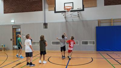 Mehrere Jugendliche spielen in einer Halle Basketball. 