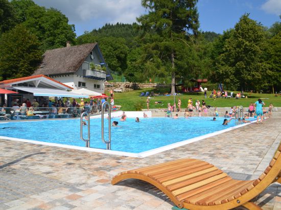 Eine Sonnenliege in einem Schwimmbad mit vielen Menschen.