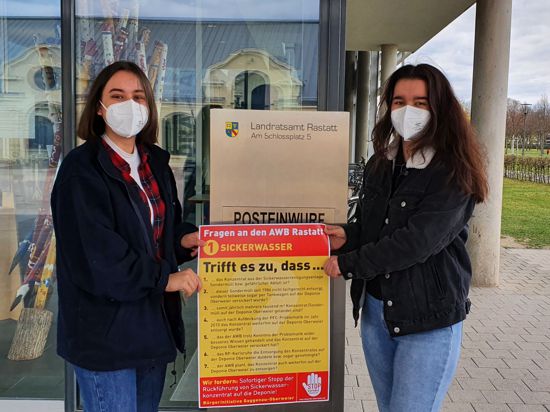 Zwei junge Frau zeigen vor dem Landratsamt in Rastatt ein Plakat mit Fragen an den Abfallwirtschaftsbetrieb zum Thema Sickerwasser auf der Deponie Hintere Dollert 