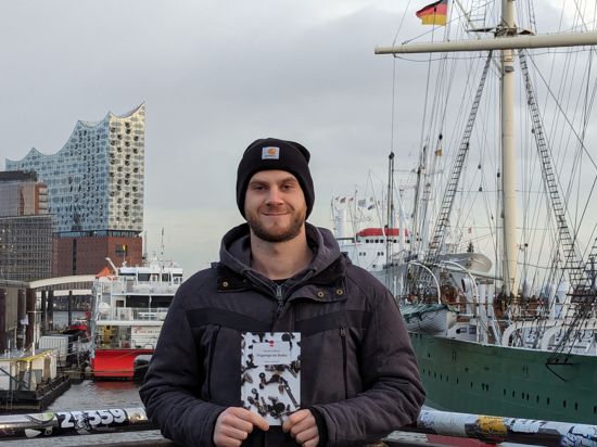Sebastian Kohlhauer steht im Hamburger Hafen vor einem Segelschiff.