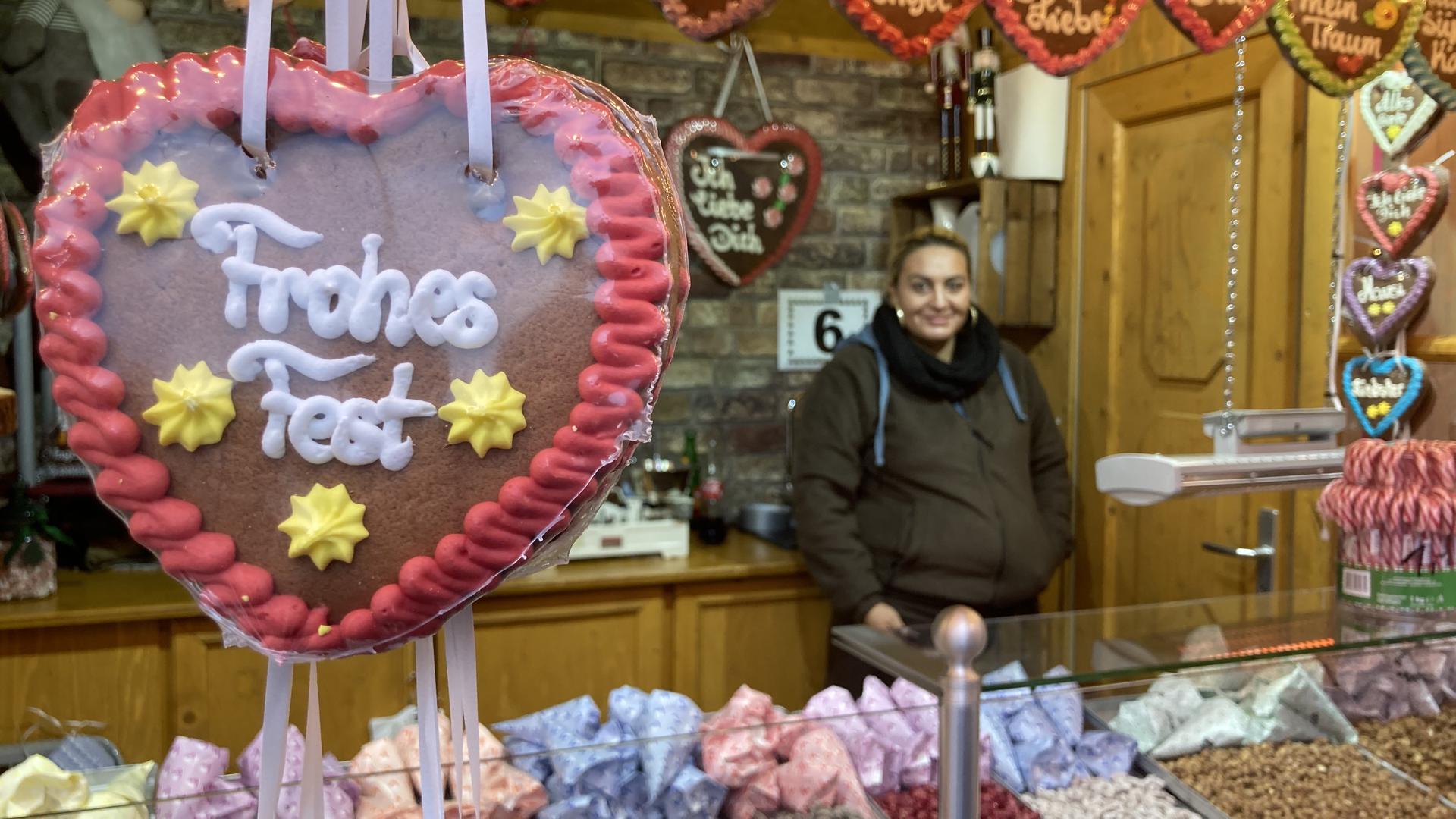 ein Lebkuchenherz mit der Aufschrift „Frohes Fest“ hängt an einem Süßwarenstand auf einem Weihnachtsmarkt.