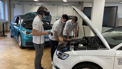 Schüler stehen mit VR-Brille an der Motorhaube eines E-Autos.