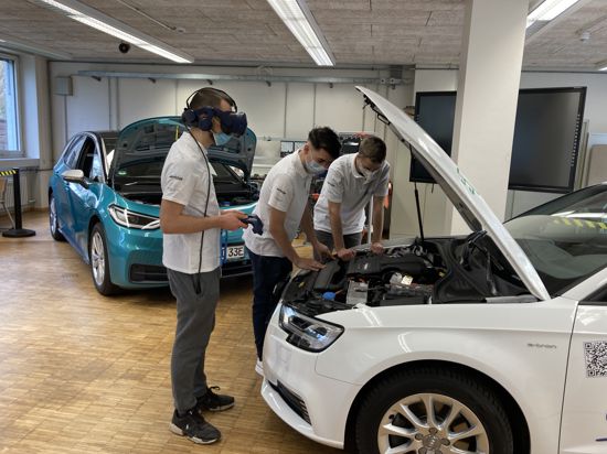 Schüler stehen mit VR-Brille an der Motorhaube eines E-Autos.