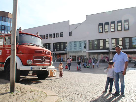 Blick auf das Kaufhaus vom Marktplatz aus. Links im Bild das rote Spielmobil des Vereins Kindgenau, ein altes Feuerwehrauto von Mercedes-Benz.