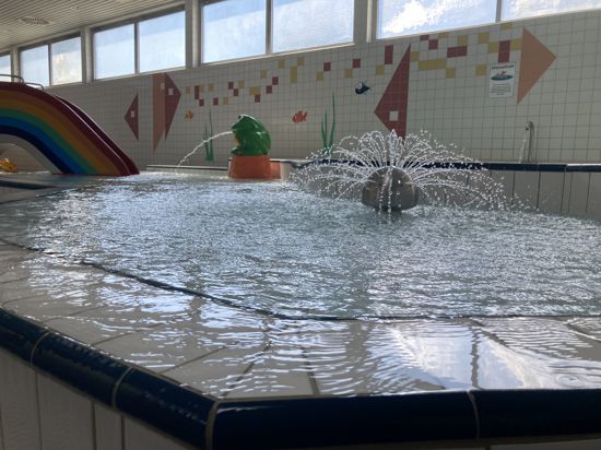 ein Kinderbecken im Schwimmbad  mit Wasserfontänen und einer Regenbogenrutsche