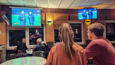 Menschen sitzen in einer Bar vor Bildschirmen