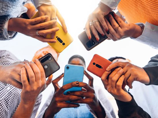 Junge Leute stehen im Kreis und halten ihr Handy vor sich. Das Foto ist von unten nach oben aufgenommen, da dass man die Hände mit den Telefonen im Vordergrund sieht und die Köpfe unscharf dahinter.