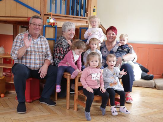 Drei Erwachsene und sieben Kleinkinder sitzen in einem kindgerecht eingerichteten Spielzimmer