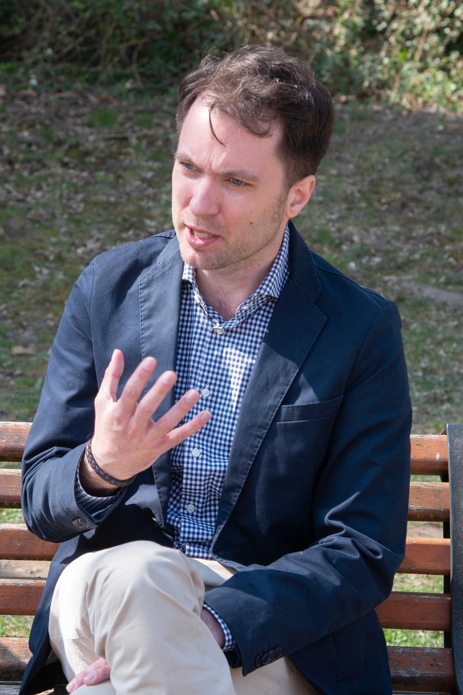 Ein Mann sitzt auf einer Parkbank und gestikuliert mit seiner rechten Hand beim Sprechen
