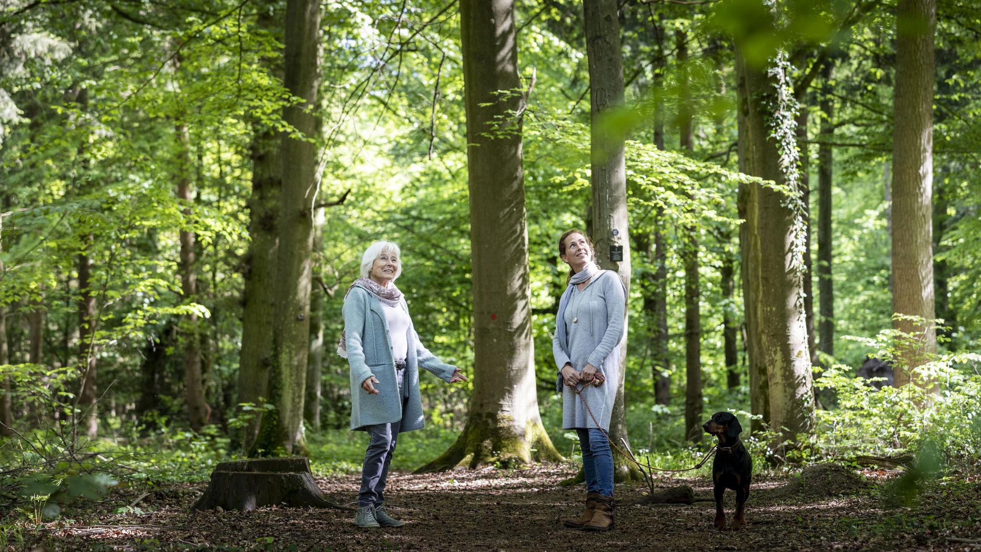 Eine jüngere und eine ältere Frau stehen mit einem Hund in einem Bestattungswald.