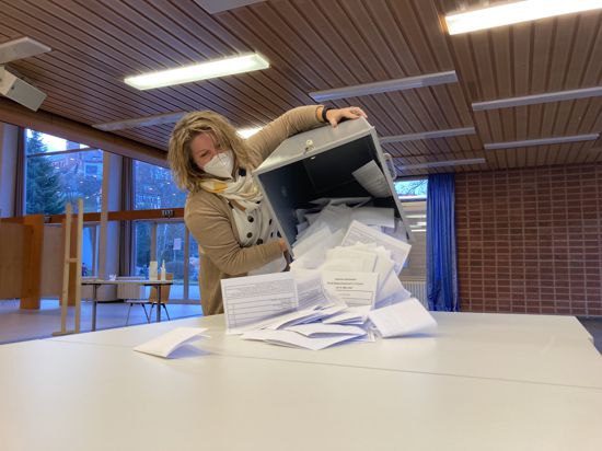 Eine Frau mit Mundschutz kippt den Inhalt einer Wahlurne auf einen Tisch