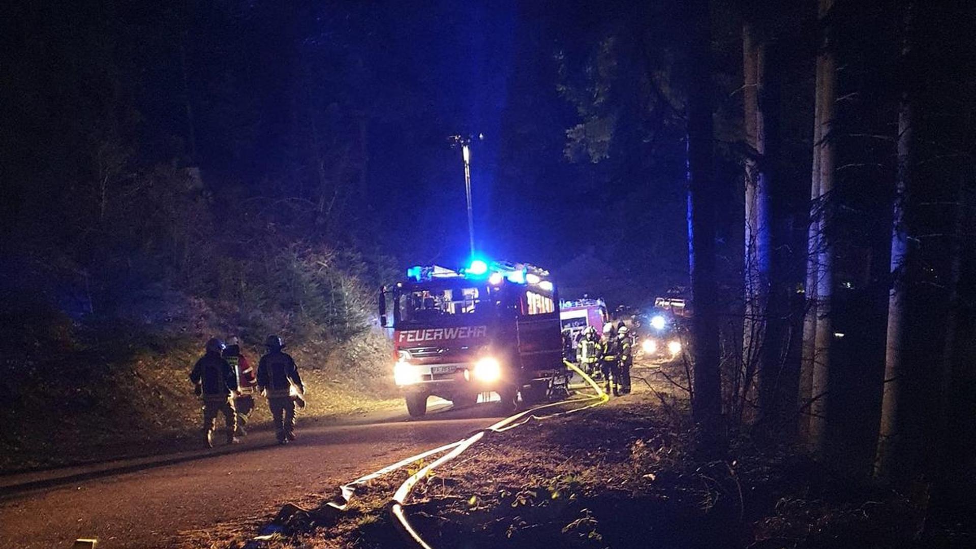 Feuerwehrautos stehen nachts in einem Wald, im Vordergrund sind ausgerollte Schläuche zu sehen.