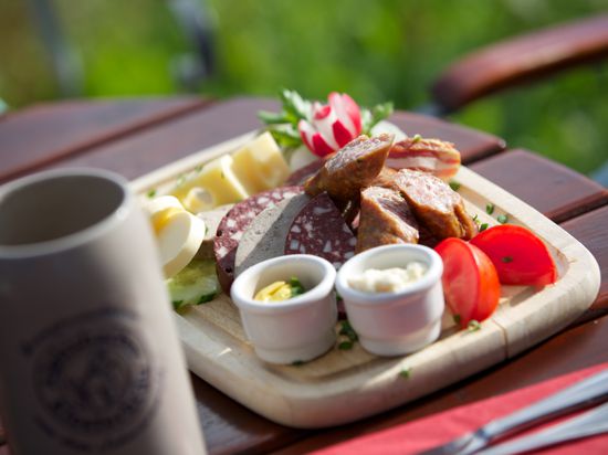 Die Vesperplatte auf dem Panoramastüble in Baiersbronn. Ein Bierkrug neben einem Holzbrett mit Wurst, Tomatenstücken, Radieschen, Butter und Brot auf einem Holztisch.