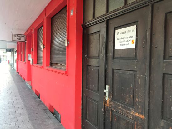 Rote Gasthausfassade, heruntergelassene Rollläden, heruntergekommenes Holztor mit einem Schild der „Einfahrt freihalten“-Schild Brauerei Franz.