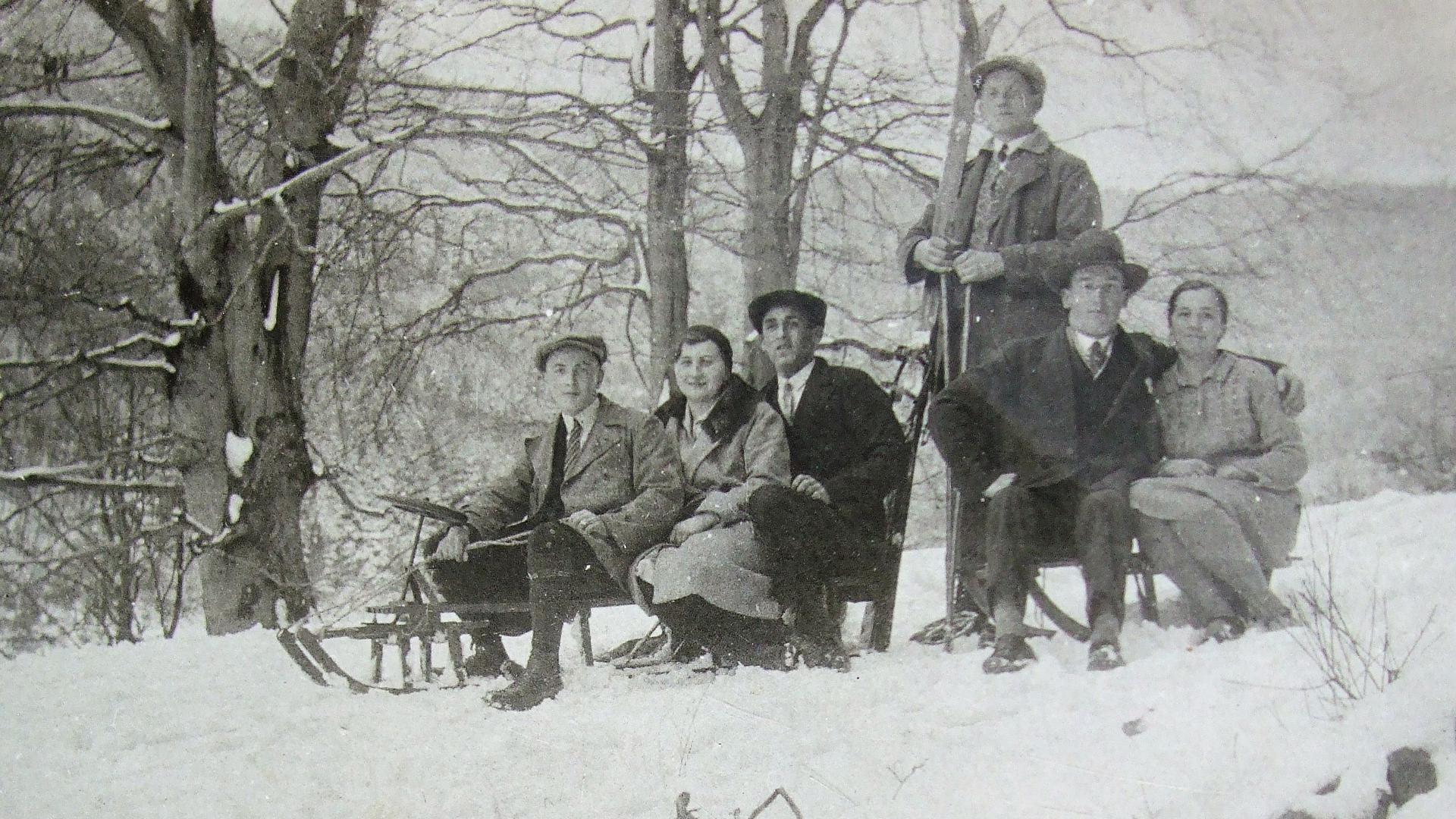 Historische Aufnahme von 1930: Zwei Schlitten mit zwei bzw. drei Personen und eine Person in der Mitte stehend mit Skiern auf einer Rodelstrecke auf dem Buchholzweg