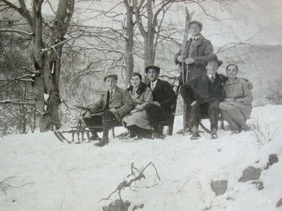 Historische Aufnahme von 1930: Zwei Schlitten mit zwei bzw. drei Personen und eine Person in der Mitte stehend mit Skiern auf einer Rodelstrecke auf dem Buchholzweg