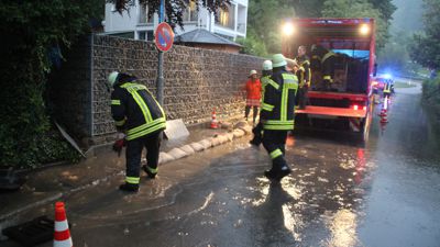Wassermassen fließen die Lautenbacher Straße in Scheuern entlang. Die Feuerwehr legt Sandsäcke an den Straßenrand.