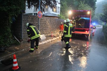 Wassermassen fließen die Lautenbacher Straße in Scheuern entlang. Die Feuerwehr legt Sandsäcke an den Straßenrand.