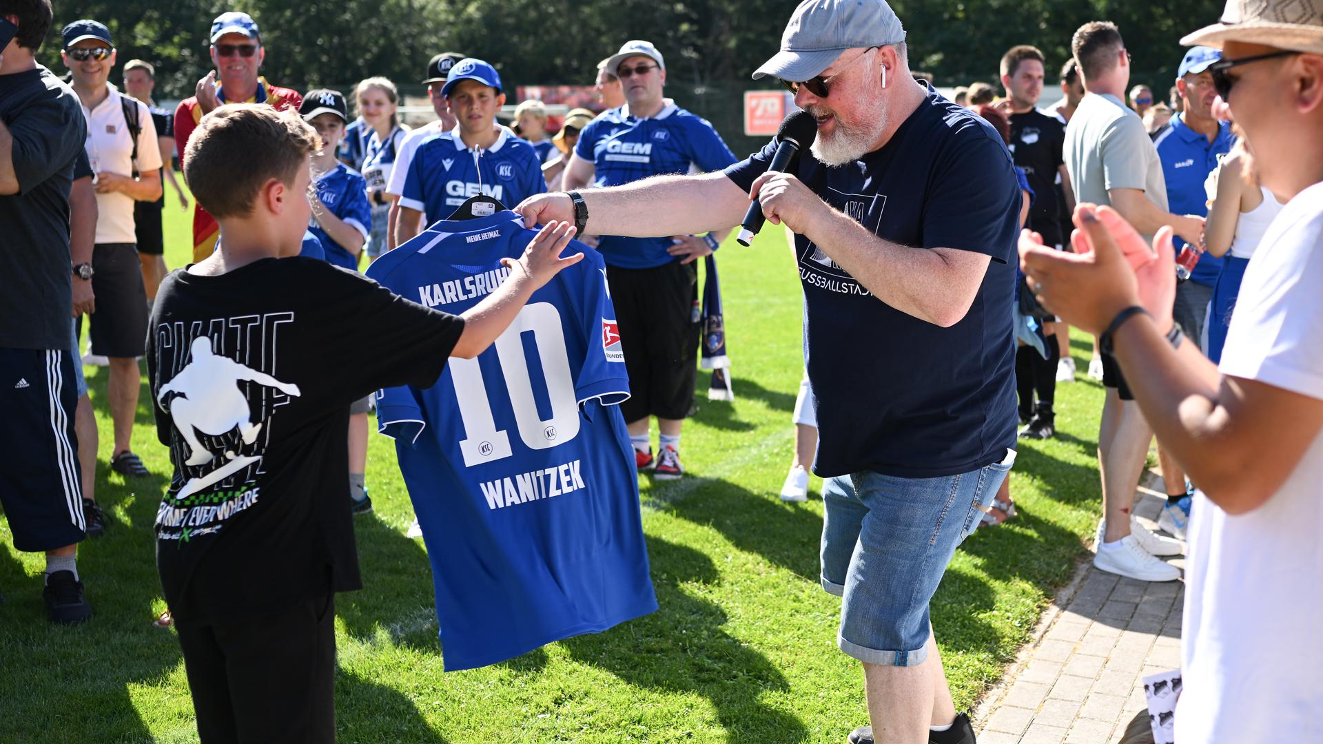 KSC-Stadionsprecher Martin Wacker übergibt einem Fan das Trikot von Marvin Wanitzek.