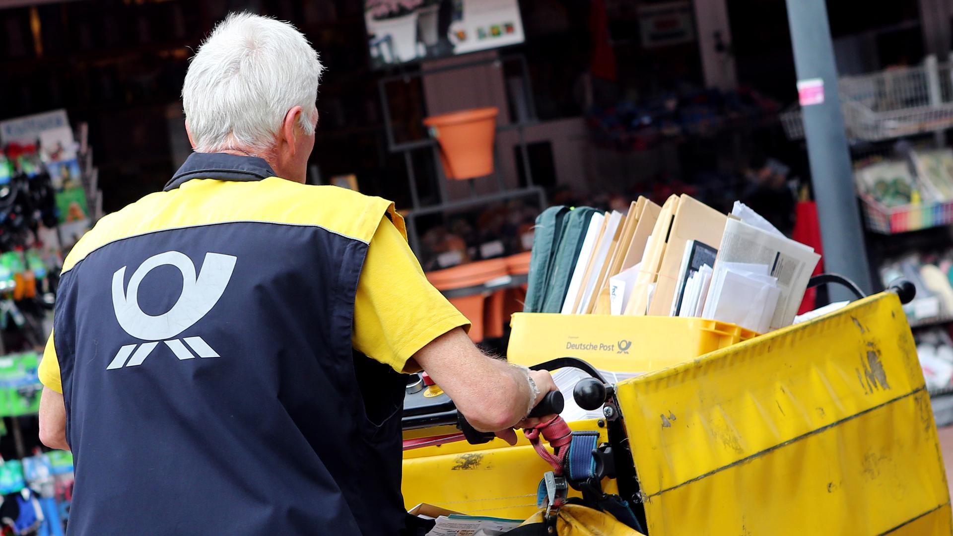 Ein Postbote schiebt einen Wagen mit Briefen über einen Platz in Hamburg. 