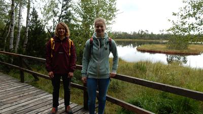 Elischa Mannal (links) und Anna Sinke in Wanderkleidung auf dem Bohlenweg am See im Hochmoorgebiet Kaltenbronn