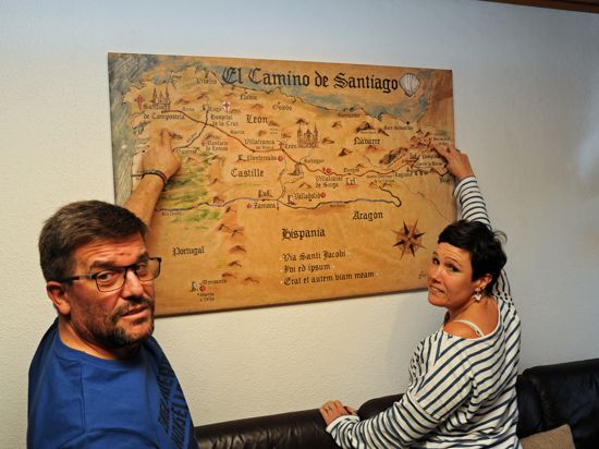 Heike und Marco Borchard zeigen in ihrem Wohnzimmer auf eine Karte, die den Jakobsweg abbildet 