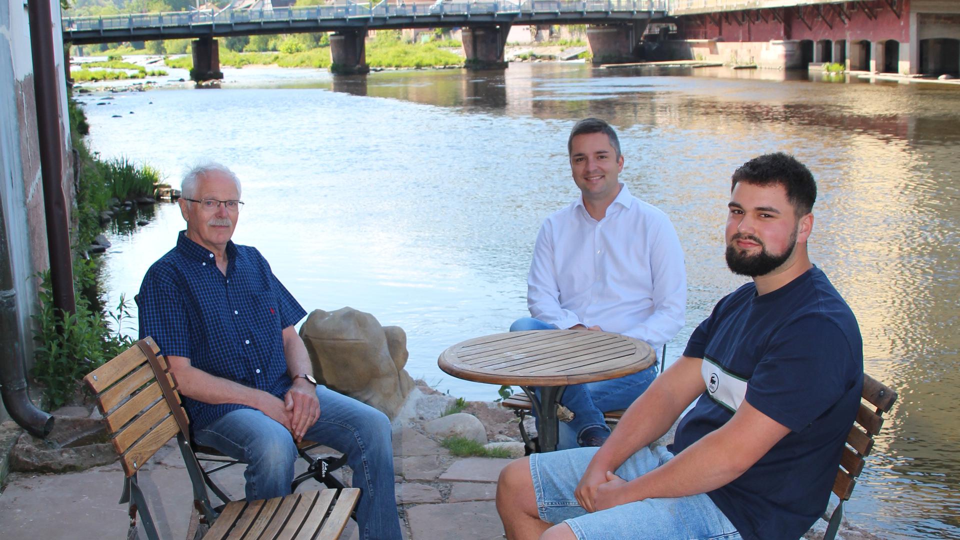 Drei Männer sitzen an einem Tisch am Ufer