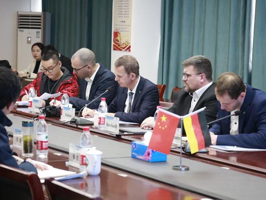 Männer sitzen an einem Schreibtisch, auf dem deutsche und chinesische Wimpel stehen.