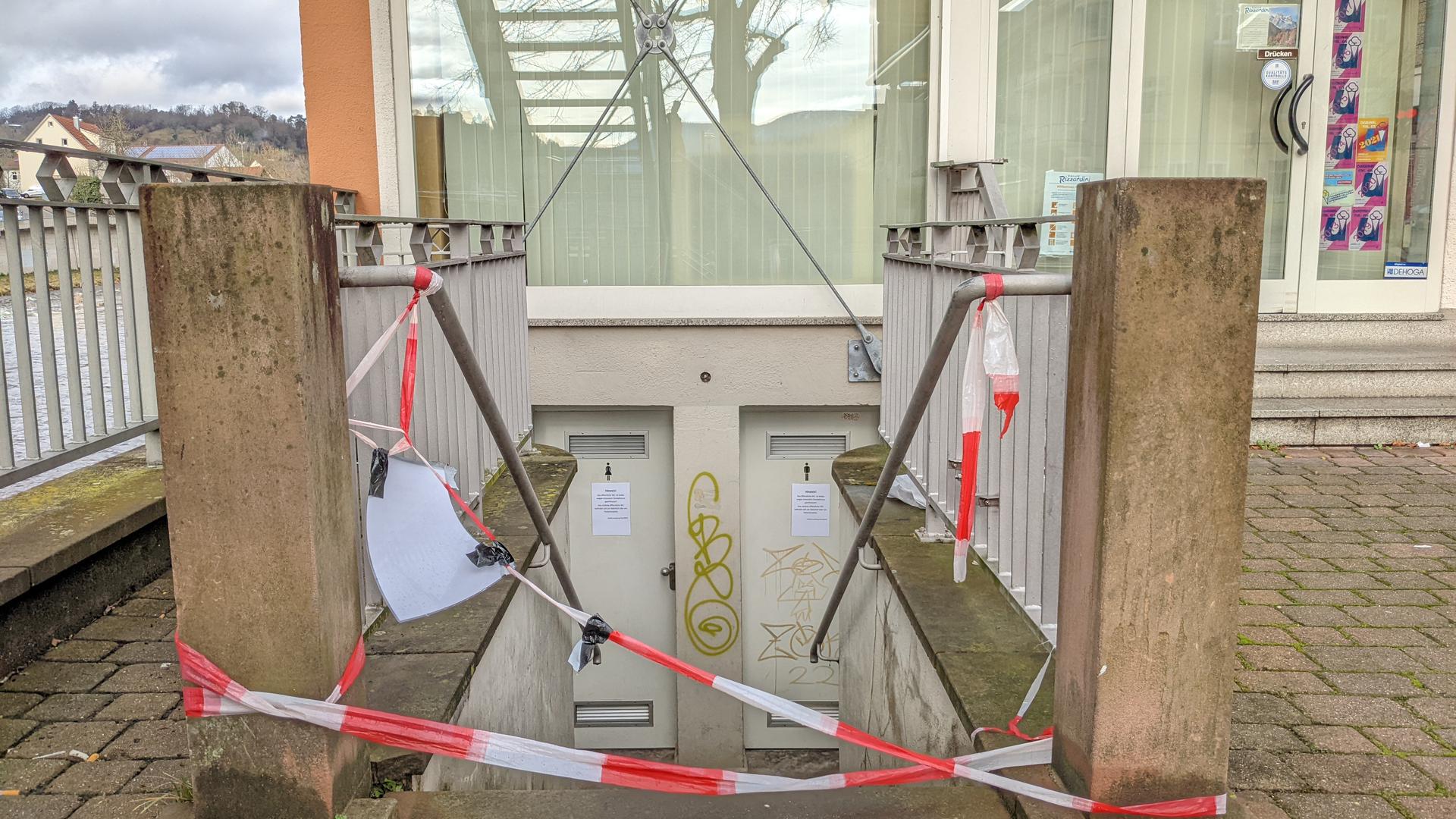 Ein rot-weißes Absperrband hängt an einer Treppe, die hinunter zu einer öffentlichen Toilette an der Gernsbacher Stadtbrücke führt.