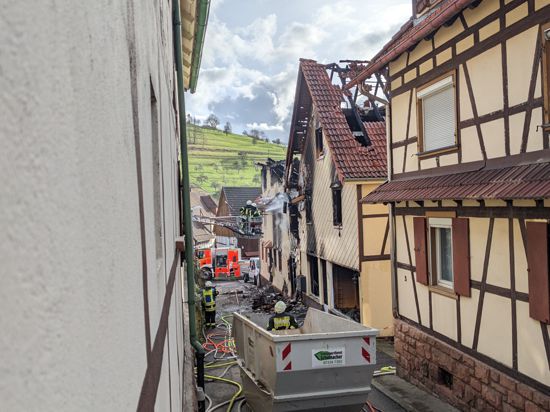 .Feuerwehrleute räumen Schutt vor einem abgebrannten Haus weg.