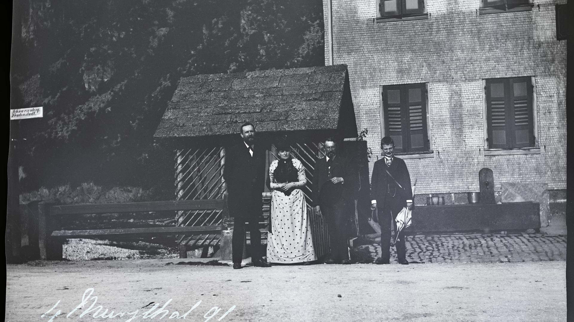 historische Aufnahme aus dem Murgtal, vier Personen, zwei Männer, eine Frau, ein Jugendlicher, stehen vor einem zweigeschossigen Gebäude auf der Schotterstraße